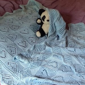 May include: A light blue crocheted baby blanket with a delicate lace pattern. A black and white panda plush toy is partially hidden under the blanket.