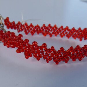 Puede incluir: Una pulsera de cuentas rojas con un cierre decorativo. La pulsera est&aacute; hecha de peque&ntilde;as cuentas rojas redondas ensartadas en un patr&oacute;n en zigzag. El cierre es de color bronce.
