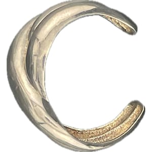 May include: A silver-toned, curved ear cuff. The cuff has a smooth, polished exterior with a textured interior. The design features a continuous, flowing shape, creating a modern and minimalist aesthetic. This piece of jewelry is designed to be worn on the ear.