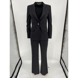 May include: A dark gray pinstripe suit, consisting of a blazer and matching pants. The blazer has a single button closure and two front pockets. The pants are flared at the bottom. The suit is displayed on a mannequin against a white background.