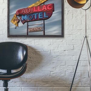 K&ouml;nnte beinhalten: Ein gerahmter Kunstdruck mit einem alten Cadillac Motel Neonschild mit roter und blauer Schrift, einem gelben Pfeil und einem kleinen rechteckigen Schild darunter mit der Aufschrift VACANCY vor einem bew&ouml;lkten Himmel in einem Raum.