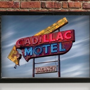 K&ouml;nnte beinhalten: Ein gerahmter Kunstdruck mit einem alten Cadillac Motel Neonschild. Das Schild zeigt die W&ouml;rter CADILLAC in rotem Neon, MOTEL in blauem Neon und ein kleineres VACANCY-Schild darunter. Ein gro&szlig;er gelber Neonpfeil zeigt vor einem bew&ouml;lkten Himmel nach unten.