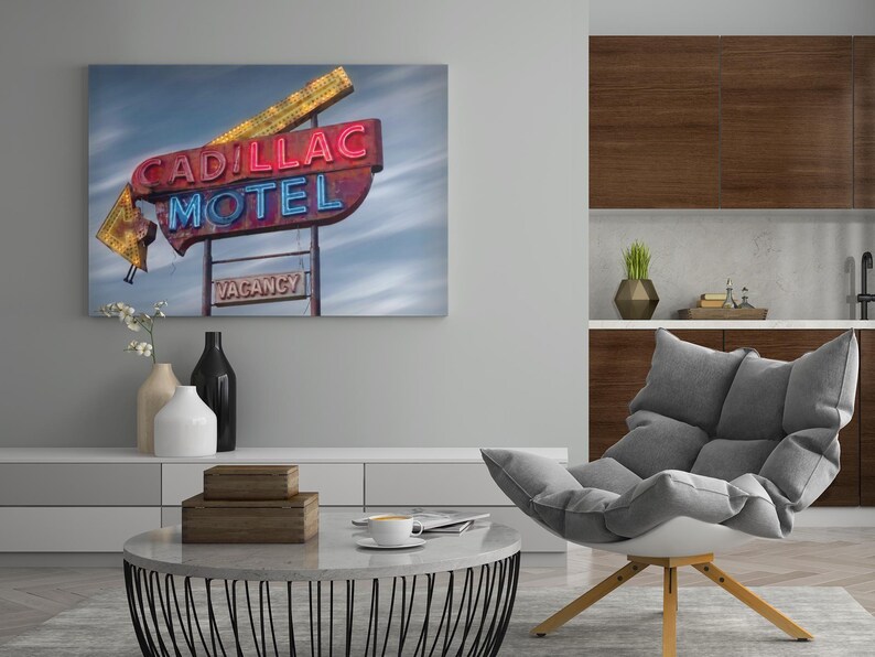 K&ouml;nnte beinhalten: Ein rechteckiger Wandkunstdruck mit einem verwitterten Neonreklameschild im Vintage-Stil, das die Aufschrift CADILLAC MOTEL in roten und blauen Buchstaben zeigt, sowie ein kleineres VACANCY-Schild darunter vor einem bew&ouml;lkten Himmel.