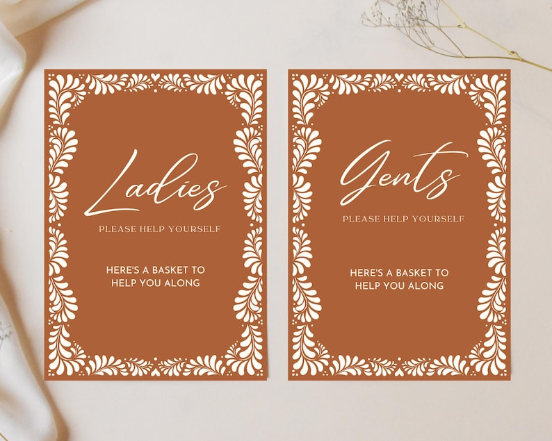 Puede incluir: Dos letreros marrones con bordes florales blancos y texto blanco. Los letreros dicen "Ladies Please Help Yourself Here's a Basket to Help You Along" y "Gents Please Help Yourself Here's a Basket to Help You Along".