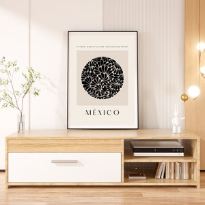 Puede incluir: Un mueble de TV de madera clara con un caj&oacute;n blanco, dos estantes y una impresi&oacute;n enmarcada en negro con un dise&ntilde;o floral en blanco y negro y la palabra "M&Eacute;XICO".