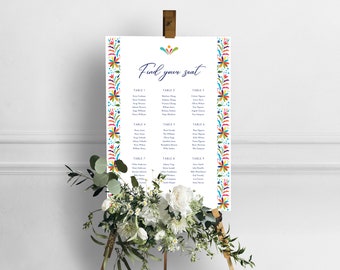 May include: A white wedding seating chart with a colorful Mexican-inspired floral border. The chart lists guest names and table numbers. The text at the top reads "Find your seat."