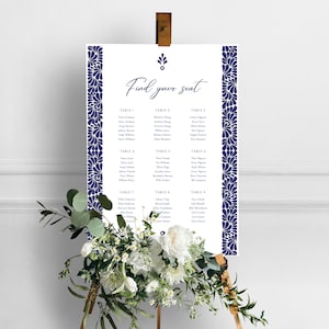 May include: A white wedding seating chart with a navy blue floral border. The chart is titled "Find your seat" and lists the names of guests assigned to each table.