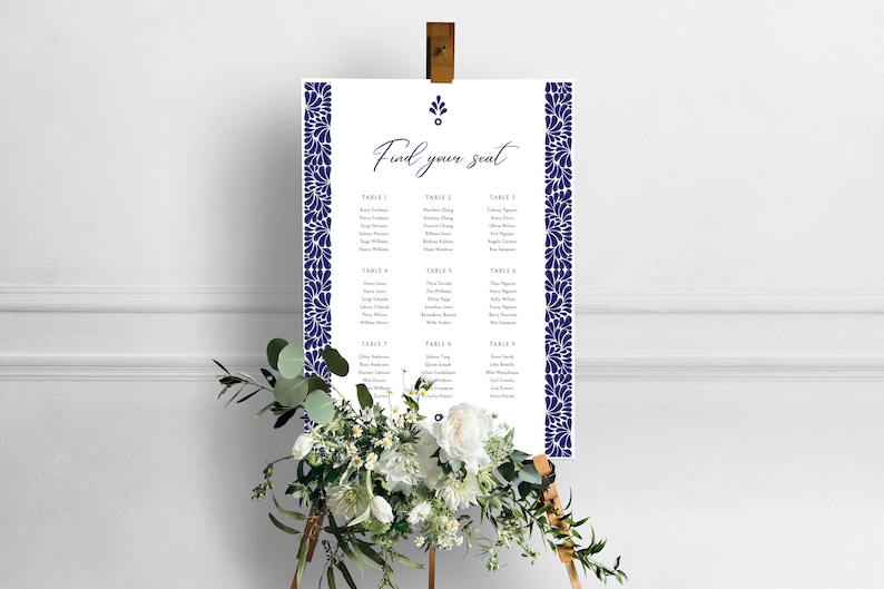 May include: A white wedding seating chart with a navy blue floral border. The chart is titled "Find your seat" and lists the names of guests assigned to each table.
