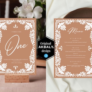 Puede incluir: Dos tarjetas marrones con diseños florales blancos. La tarjeta de la izquierda es una tarjeta de número de mesa con el número "Uno" y el texto "Table No." La tarjeta de la derecha es una tarjeta de menú con el texto "Menu" y los encabezados "Entrada", "Plato principal" y "Postre".