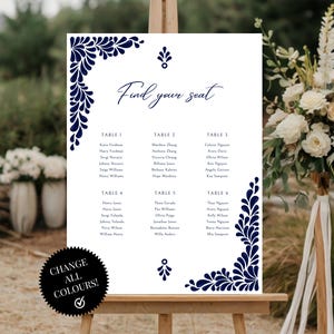 Peut inclure: Un tableau de mariage blanc avec un motif floral bleu marine. Le tableau est intitul&eacute; "Trouvez votre place" et liste les noms des invit&eacute;s assign&eacute;s &agrave; chaque table. Le tableau est affich&eacute; sur un chevalet.