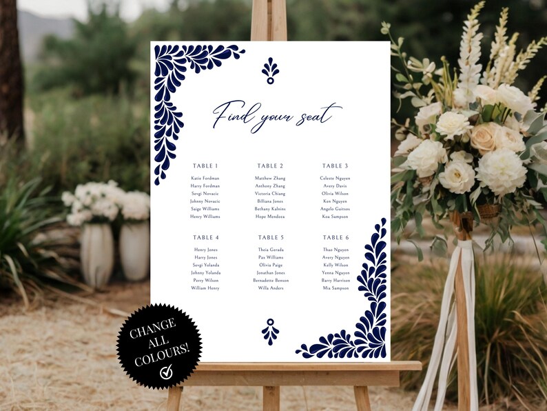Peut inclure: Un tableau de mariage blanc avec un motif floral bleu marine. Le tableau est intitul&eacute; "Trouvez votre place" et liste les noms des invit&eacute;s assign&eacute;s &agrave; chaque table. Le tableau est affich&eacute; sur un chevalet.