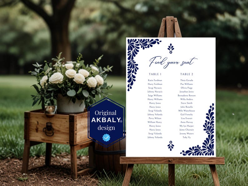 Peut inclure: Un tableau de mariage blanc avec des motifs floraux bleus. Le tableau est intitul&eacute; "Find your seat" et liste les noms pour deux tables, Table 1 et Table 2.