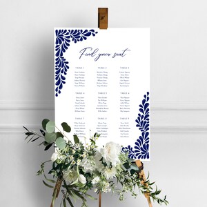 Peut inclure: Un plan de table de mariage blanc avec un motif floral bleu marine. Le tableau est intitul&eacute; "Trouvez votre place" et liste les noms des invit&eacute;s assign&eacute;s &agrave; chaque table.