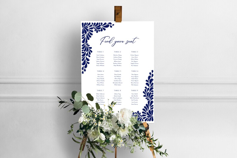 Peut inclure: Un plan de table de mariage blanc avec un motif floral bleu marine. Le tableau est intitul&eacute; "Trouvez votre place" et liste les noms des invit&eacute;s assign&eacute;s &agrave; chaque table.