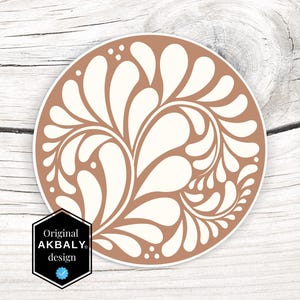 Puede incluir: Una pegatina redonda con fondo marrón y un diseño floral blanco. El diseño presenta un patrón de hojas y flores en espiral.
