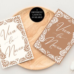 May include: Two printable designs for a wedding sign. The sign says "Viva la Novia" in a decorative script font. The designs feature a brown background with a white floral pattern.