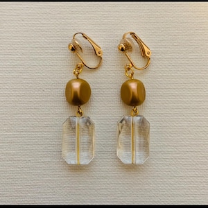 May include: Gold tone clip-on earrings with a clear faceted rectangular bead and a gold round bead.