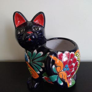 May include: A black ceramic cat planter with colorful floral designs. The planter has a wide opening for planting and a black glazed finish.