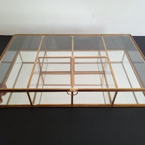 May include: A rectangular display box featuring a gold-toned metal frame and clear glass panels. The interior is divided into six equal compartments by thin metal dividers, and the base of the box is lined with a reflective mirror surface.