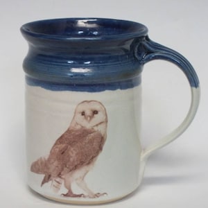 May include: A white ceramic mug with a blue rim and handle. The mug features a brown and white barn owl illustration.