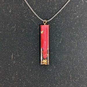 May include: A red and gold resin pendant necklace with a rectangular shape. The pendant has gold flecks embedded in the red resin.