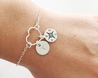 Puede incluir: Un brazalete de cadena de plata con un dije en forma de corazón y dos dijes redondos. Un dije tiene una brújula con las direcciones N, S, E y W. El otro dije tiene la letra T.