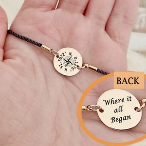 Puede incluir: Un brazalete de cordón negro con dos dijes dorados. El dije delantero presenta una brújula con coordenadas y el dije trasero dice "Where it all Began".
