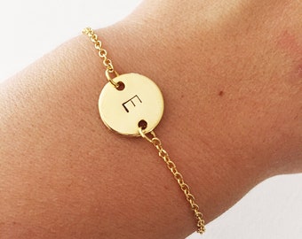 May include: A gold chain bracelet with a round charm featuring the letter "E" engraved on it.