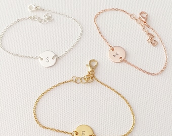 May include: Three delicate chain bracelets with a round charm featuring a single letter. The bracelets are silver, rose gold, and gold, and the charms are engraved with the letters S, I, and E.