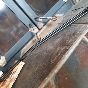 May include: A pair of black metal fireplace tools with a coiled handle. The tools are lying on a wooden surface and a stone floor.