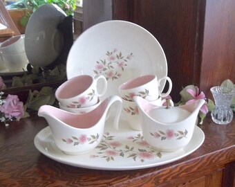 May include: A set of white and pink floral patterned china teacups and saucers with a matching creamer and sugar bowl. The set is displayed on a white oval serving tray.