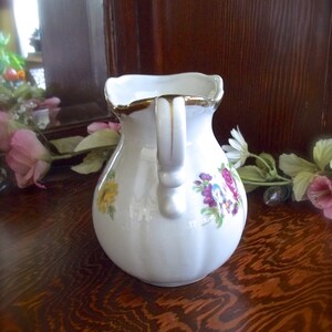 Peut inclure: Une cr&eacute;mier en c&eacute;ramique blanche avec un bord dor&eacute; et un motif floral. La cr&eacute;mier a une poign&eacute;e avec un accent dor&eacute;.