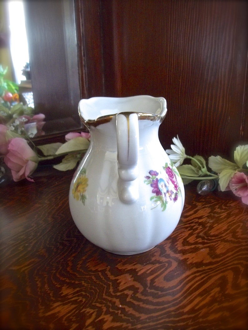 Peut inclure: Une cr&eacute;mier en c&eacute;ramique blanche avec un bord dor&eacute; et un motif floral. La cr&eacute;mier a une poign&eacute;e avec un accent dor&eacute;.