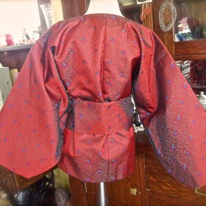 K&ouml;nnte beinhalten: Ein rotes Kimono mit einem blauen und goldenen Blumenmuster. Das Kimono hat lange &Auml;rmel und einen G&uuml;rtel.