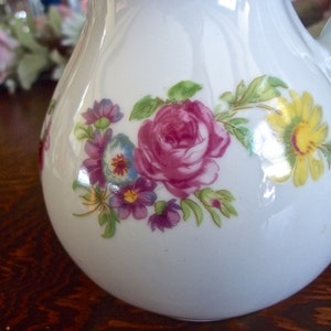 Peut inclure: Pichet en c&eacute;ramique blanche avec un motif floral compos&eacute; de fleurs roses, jaunes et violettes. Le pichet a une anse et un corps en forme de poire.
