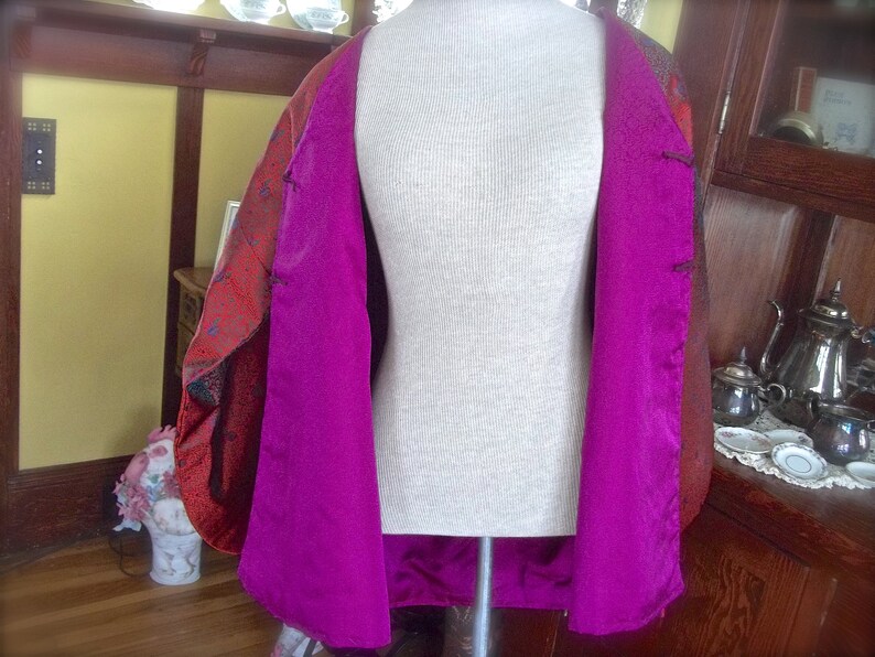 K&ouml;nnte beinhalten: Eine rot-schwarze gemusterte Jacke mit magentafarbenem Futter. Die Jacke ist offen und das Futter ist sichtbar. Die Jacke befindet sich auf einer wei&szlig;en Schaufensterpuppe.
