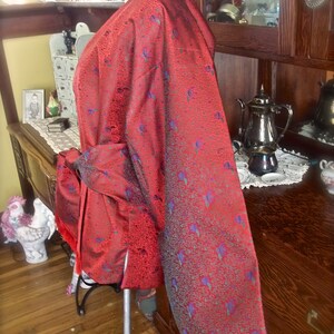 K&ouml;nnte beinhalten: Ein rot-blaues gemustertes Kimono mit einem langen, flie&szlig;enden &Auml;rmel. Das Kimono ist aus einem seidenartigen Stoff gefertigt und hat einen dezenten Glanz.