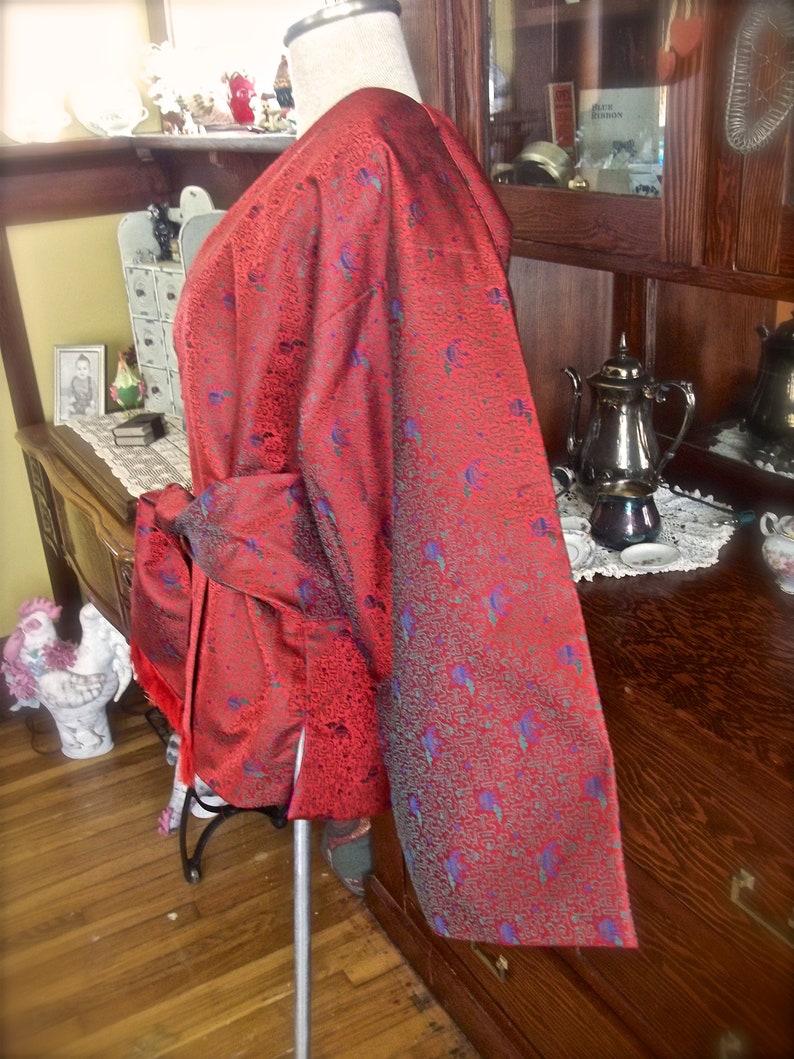 K&ouml;nnte beinhalten: Ein rot-blaues gemustertes Kimono mit einem langen, flie&szlig;enden &Auml;rmel. Das Kimono ist aus einem seidenartigen Stoff gefertigt und hat einen dezenten Glanz.