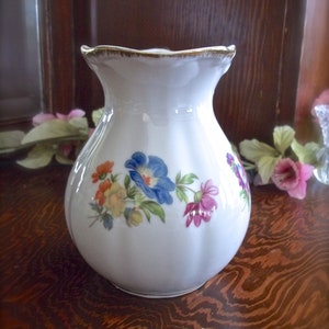 Peut inclure: Un vase en c&eacute;ramique blanche avec un bord festonn&eacute; et un motif floral. Le vase pr&eacute;sente une vari&eacute;t&eacute; de fleurs dans des tons de rose, bleu, jaune et orange.