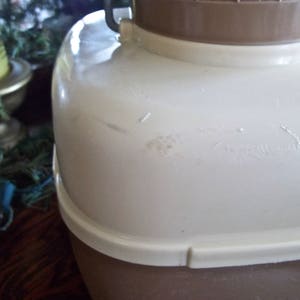 May include: A white and brown insulated beverage container with a lid and a handle. The container has a small scratch on the side.