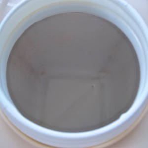 May include: Close-up view of the inside of a white plastic container with a beige interior. The container has a round opening and a smooth, slightly textured surface.