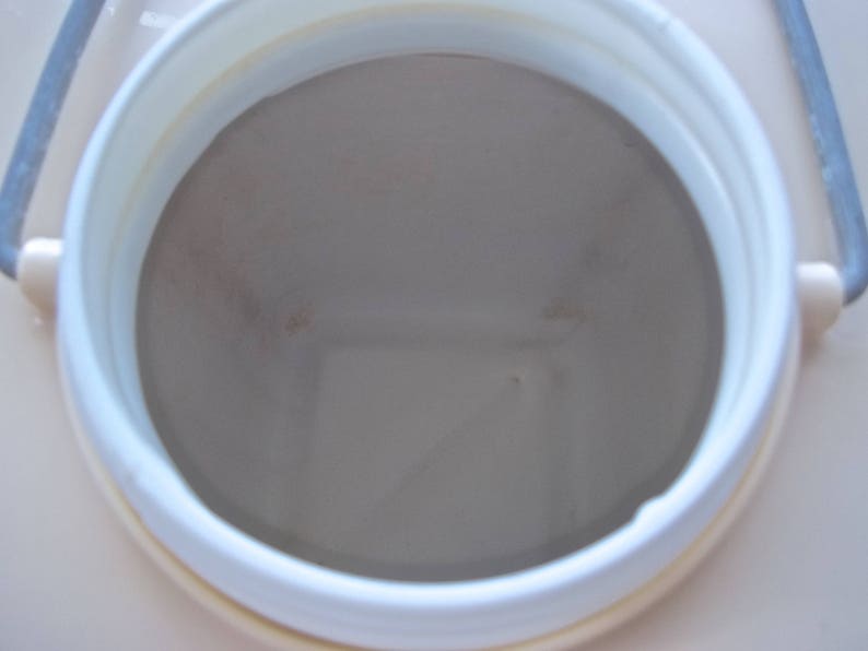 May include: Close-up view of the inside of a white plastic container with a beige interior. The container has a round opening and a smooth, slightly textured surface.