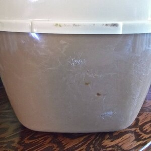 May include: A vintage, off-white and brown plastic container with a lid. The container has a smooth, slightly textured surface with some scratches and marks.