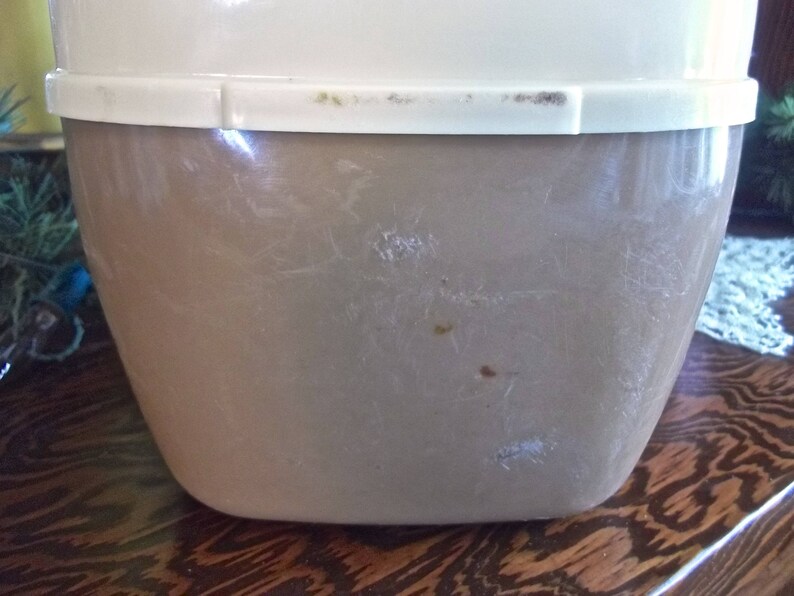 May include: A vintage, off-white and brown plastic container with a lid. The container has a smooth, slightly textured surface with some scratches and marks.