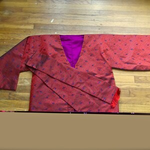 K&ouml;nnte beinhalten: Ein rotes und violettes Kimono mit einem Blumenmuster. Das Kimono hat einen langen, flie&szlig;enden &Auml;rmel und eine Sch&auml;rpe, die sich in der Taille bindet.