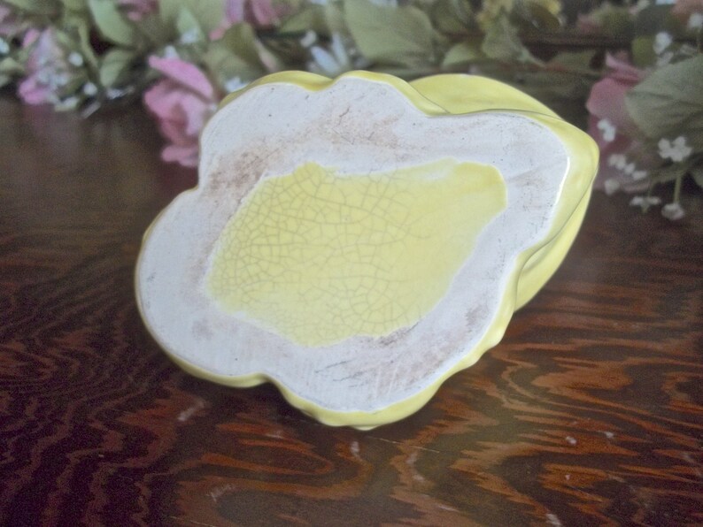 May include: A vintage, yellow ceramic dish with a scalloped edge. The base is a light yellow with a cracked glaze pattern. The rim is white with a slightly aged appearance. The dish is likely a decorative or serving piece.