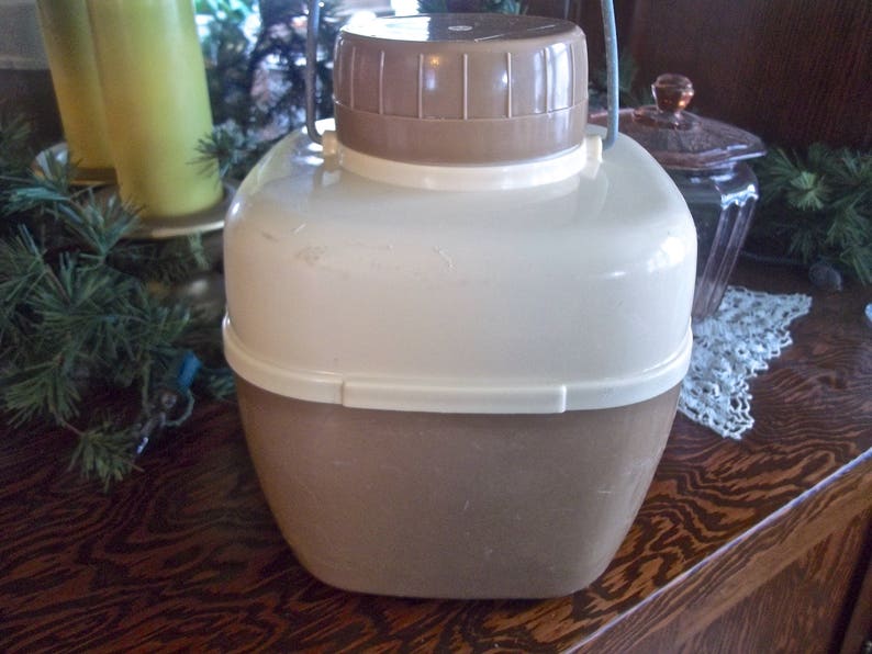 May include: A vintage brown and white plastic insulated beverage pitcher with a lid and a handle. The pitcher has a textured surface and a slightly rounded shape.