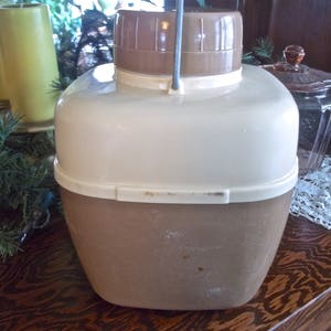 May include: A vintage brown and white insulated beverage dispenser with a metal handle. The dispenser has a white lid and a brown body.