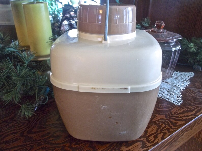 May include: A vintage brown and white insulated beverage dispenser with a metal handle. The dispenser has a white lid and a brown body.
