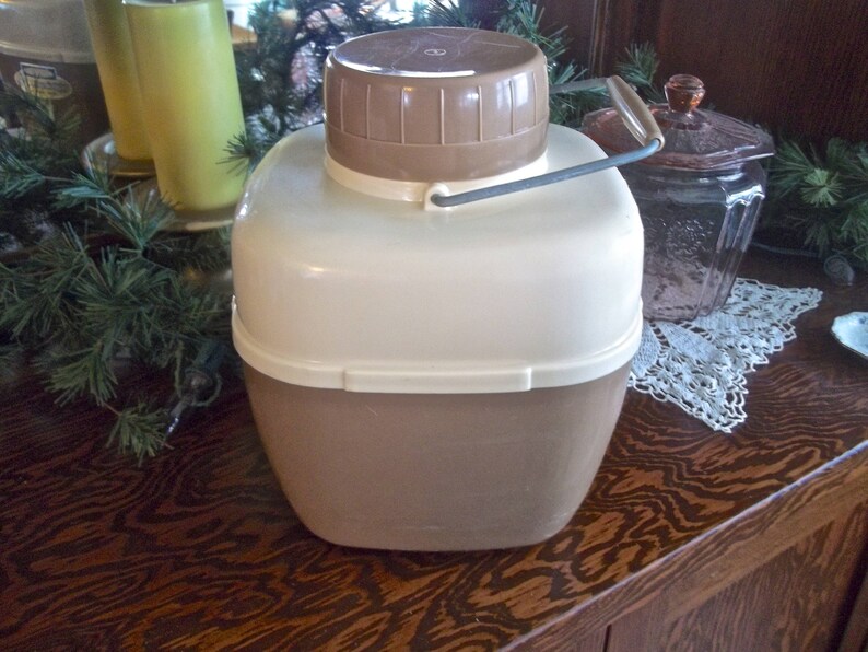 May include: A brown and white insulated beverage container with a lid and a handle. The container has a white top and a brown bottom.